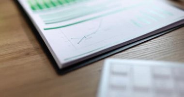 Ofisteki ahşap masanın üzerinde dosya kağıtları ve modern beyaz hesap makinesi olan klasör. İş yerinde muhasebe malzemeleri ve elektronik cihaz
