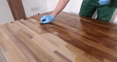 Marangoz, ahşap döşeme yüzeyi işliyor. Zemin vernikle renklendiriyor. Lastik eldivenli adam oturma odası için parke parlatıyor.