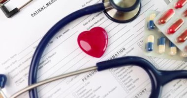 Steteskoplu kırmızı kalp oyuncağı ve haplar klinikteki hastanın tıbbi geçmişinde yatıyor. Tıbbi ekipman ve kalp hastalıkları konsepti