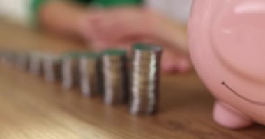 Seramik domuz kumbarası ahşap masanın üzerine yerleştirilmiş bozuk para yığınlarının yanında duruyor. Tasarruf ve birikim için küçük para konteynırı