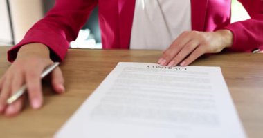 Kadın girişimci, ahşap masada otururken imzalaması için ortağına sözleşme kağıdı veriyor. Pembe ceketli kadın ağır çekimde anlaşma yapıyor.