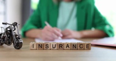 Masada potansiyel risk olarak motorsiklet modelinin yanındaki tahta küplerden yapılmış kelime sigortası. Yeşil ceketli kadın çalışan, ağır çekimde sözleşme imzaladı.