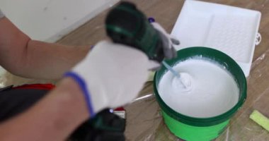 İnşaatçı, odanın zemininde elektrikli mikserle kovada sıvı boya karıştırıyor. İşçi ev bakımı için malzeme hazırlar. Ev yenilenmesi