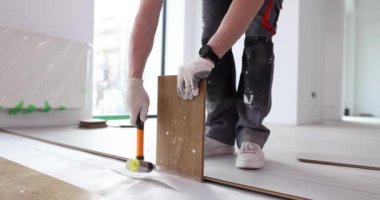 İnşaatçı, inşaat alanının zeminine çekiçle çekiçle vurulan laminat tahtalarını tamir ediyor. Adam odaya zemin örtüsü kuruyor. Bitirme çalışmaları