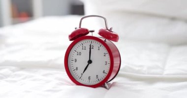 Red alarm clock for seven in morning is on bed. Morning awakening and sleep concept