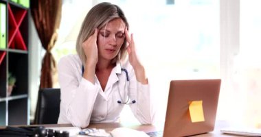 Masada oturan yorgun kadın doktor, elinde filmle şakağa masaj yapıyor. Tıbbi personel kavramının duygusal çöküntüsü