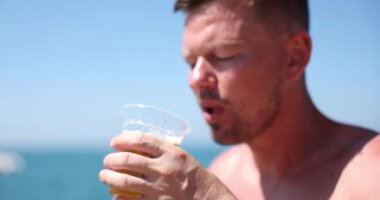 Young man drinking cold beer on summer beach. Handsome man enjoying a cold beer in the sultry heat of summer