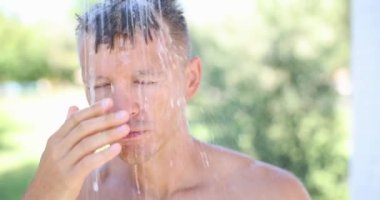 Young handsome man takes summer shower outdoor.