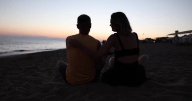 Husband and wife are sitting on beach daughter runs up to and hugs them at sunset. Family happy vacation and sea