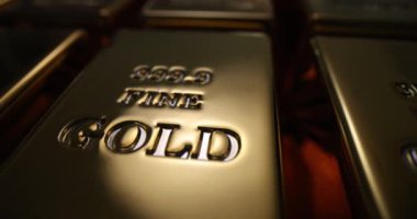 Cilalanmış altın külçeleri titizlikle düzenli sıralara dizilmiş. Değerli altın külçeler ışığı yansıtır ve loş ışıklı banka deposunda altın parıltı yaratır.