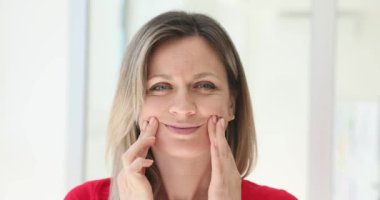 Kadın, evde ağır çekimde mutluymuş gibi davranarak parmaklarıyla dudaklarını kaldırıyor. Depresyon hastası bir kadın, acılarını gülümsemenin arkasına saklar.