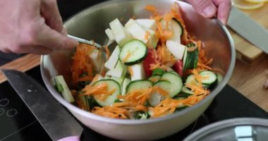 Adam metal kasede sebze salatasıyla kaşığı karıştırıyor. Şef, aile yemeği için evde sağlıklı yemekler pişiriyor. Ağır çekimde doğranmış malzemeleri birleştiriyor.