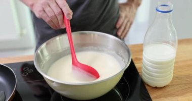 Erkek aşçı, plastik kaşıkla krep hamuru topluyor. Sobanın yanındaki adam malzemeleri karıştırıyor ve tavanın yavaş çekimde ısınmasını bekliyor.