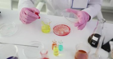 Bilim adamı, petri kabına pipetle sarı sıvı eklemiş. Laboratuvar önlüğü giyen araştırmacı, mikroorganizmaların sıvı yavaş çekime olan tepkisini gözlemliyor.