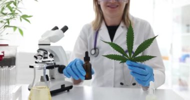 Laboratuvar önlüklü kadın bilim adamı marihuana yaprağı gösteriyor. Profesyonel araştırmacı marihuananın yavaş çekim özelliklerini inceliyor.