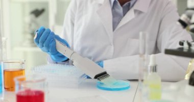 Kadın bilim adamı özel bir aletle sıvıları konteynıra boşaltıyor. Kadın laboratuarda reaksiyonları ve özellikleri gözlemlemek için deneyler yapıyor.