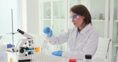 Kadın laboratuvar çalışanı sıvıyı karıştırmak için matarayı dikkatlice hareket ettiriyor. Kadın, doğru bilimsel sonuçları garanti altına almak için kontrollü koşulları sürdürüyor