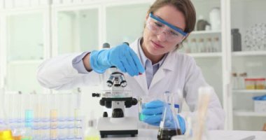 Kadın araştırmacı güçlü bir mikroskop altında detaylı analiz için sıvı hazırlıyor. Bilimadamları çeşitli laboratuvar aletleriyle çevrili.