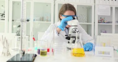 Kadın araştırmacı örneği modern mikroskop kullanarak inceliyor. Bilim adamı mikroskobun görüntülenebilirliğini artırmak için büyütülmesini ayarladı