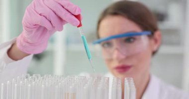Kadın bilim adamı deney tüplerine sıvı aktarmak için pipet kullanıyor. Profesyonel araştırmacı test tüplerine yavaş çekimde sıvı ekler.
