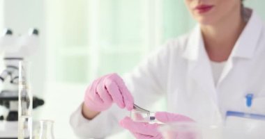 Kadın araştırmacı tabletin şeklini ve boyutunu inceliyor. Beyaz önlüklü uzman bilim adamı, ağır çekimde hapların bileşimini incelemeye hazırlanıyor.