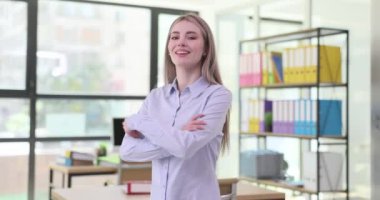 Neşeli genç kadın modern ofiste ağır çekimde kollarını kavuşturuyor. Gülümseyen mutlu kadın işçi kendine güvenini gösterir.