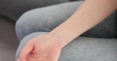 Kadın işaret ve orta parmaklarını bileğine koyup nabzını yavaş çekimde kontrol ediyor. Kadın kalp atışlarını izliyor. Evdeki kanepede oturmaktan yoruluyor.