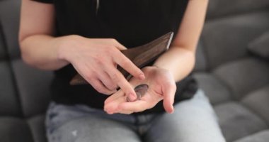 Kadın elinde deri cüzdan, elinde bozuk paraları sayıyor koltukta ağır çekimde oturuyor. Düşük ücretli meslekten dolayı para sıkıntısı çeken kadınlar