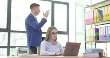 Kadın asistan, işyerindeki dizüstü bilgisayarında yazan erkek patronu dinliyor. Kadınlar görevlerini katı talimatlara göre yerine getirirler.