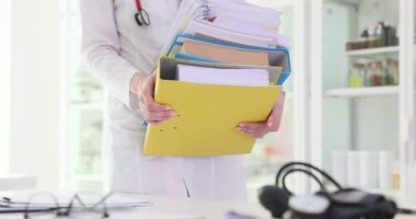Kadın doktor hastane ofisindeki masanın üzerine yığınla kağıt koyar. Sağlık çalışanı, klinikteki görevlerinden biri olarak hasta kayıtlarını hazırlar.