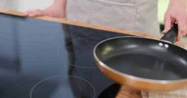 Genç bir kadın evde kızartma tavasının açık olduğu bir yerde çalışıyor. Ev hanımı, ocağı aile toplantısı için yemek hazırlamaya ayarlıyor.