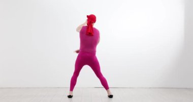 Kırmızı taytlı adam stüdyoda dinamik dans gösterisi yapıyor. Erkek dansçı her hareketinde esneklik ve ritim göstermeye çalışır.