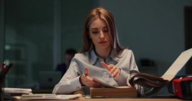 Kadın denetçi, akşam iş yerinde oturan belgeleri inceliyor. Genç bayan işçiler finansal operasyonları titiz bir şekilde kontrol ederler.