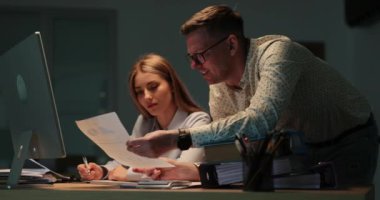 Erkek iş arkadaşı, akşam iş yerinde kadın muhasebeciye rapor veriyor. İnsan hesaplamaları kontrol etmek için hesap makinesi sunar