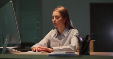 Kadın şirket çalışanı, gece geç saatlerde iş yerinde bilgisayar başında oturuyor. Adam raporları dosyalara koyar, kadın kağıtları karıştırır.