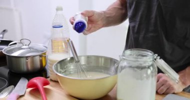 Adam mutfaktaki sıvı malzemelerle şişeden metal kaseye tuz döküyor. Adam öğle yemeği için yavaş çekimde lezzetli yemekler pişiriyor.