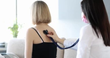 Kadın doktor, hastayı steteskopla dinler. Ev ziyareti sırasında kalp atışlarını ve akciğerlerini inceler. Covid-19 salgını sırasında doktor ev ziyareti