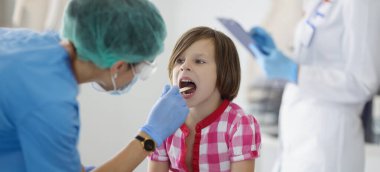 Klinikteki doktor küçük bir kızın boğazına bakıyor. Yakın plan, bulanık. Çocuk doktorunun çocuk muayenesi, teşhis