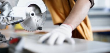 Eldivenli, yuvarlak testerenin yanındaki erkek elleri, yakın plan, bulanık. Ahşap atölyesi, testereler, marangoz ekipmanları.