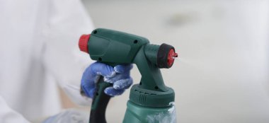 Eldivenli ellerde sprey tabanca, yakın plan, bulanık. Elektrikli inşaat aleti. Duvar kaplaması, oda yenilemesi.