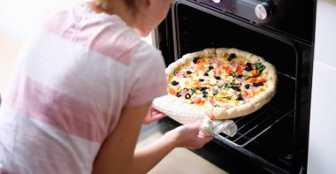 A woman takes out a round homemade pizza from the oven, close-up. Home kitchen appliances for cooking