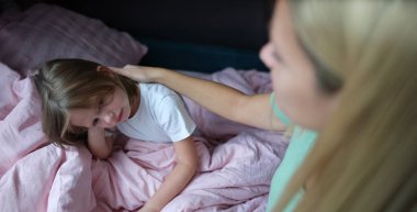 Mom stroking a frustrated little girl on the bed, close-up, blurry. Sad child, insomnia, bad dream, anxiety