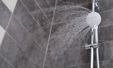 Water is pouring from the shower head into the shower room, close-up. Refreshing shower, cleanliness and hygiene