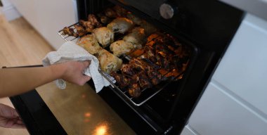 A woman takes out ready-made chicken wings and legs from the oven, close-up. Crispy chicken meat, home cooking