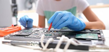 Repairman hands hold screwdrivers over laptop microcircuit, close-up, blurry. Replacing parts, upgrading an electronic device