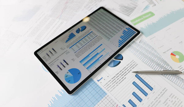 На статистических документах лежит планшет с диаграммами на экране крупным планом. Бенчмаркинг, финансовые показатели, аудит