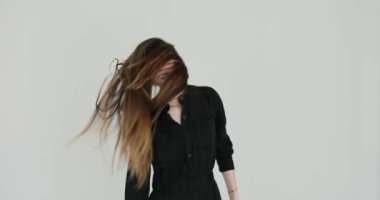 Kafasını eğen kadın, gri arka planda uzun gevşek saçların sallanmasına neden olur. Genç bayan manken saçı sofistike ve zarif bir şekilde hareket eder.