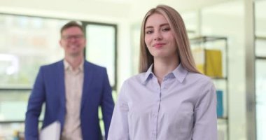 Erkek ve kadın çalışanlar ofis odasında yan yana duruyorlar. Erkek ve kadının kendine güveni ve profesyonelliği yavaş çekimde yansıtır.