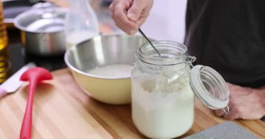 Erkek el kepçesi kavanozdan un metal kaseye dökülmesini sağlar. Adam mutfak tezgahında duran lezzetli tatlıları pişirmek için hamur hazırlıyor.