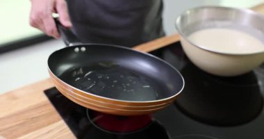 Erkek el, kızgın tavayı tutuyor ve yüzeyde daireler çizerek yağ yayıyor. Adam kahvaltıda lezzetli krepler pişirmeye hazırlanıyor.